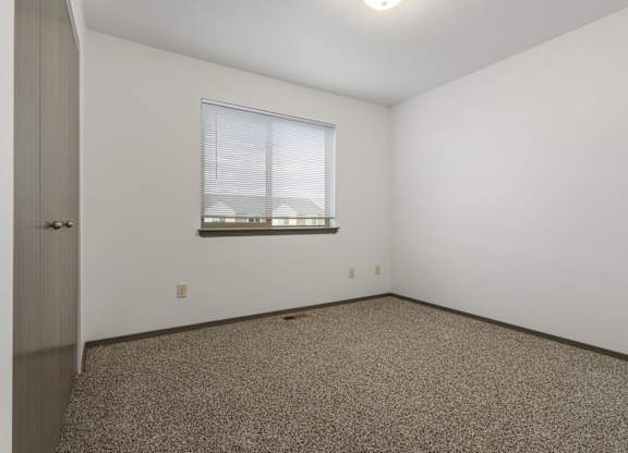A room with a carpeted floor and a window with blinds.