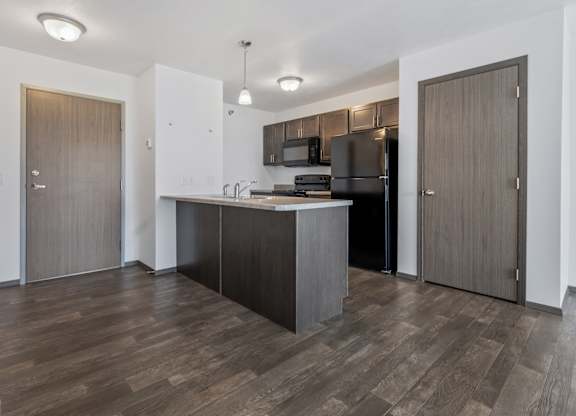 A kitchen with a black refrigerator and wooden floors.