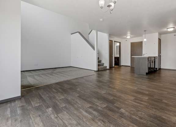 A spacious room with wooden flooring and a kitchen area in the background.