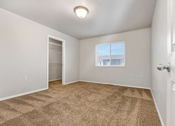 A room with a carpeted floor and a window with blinds.