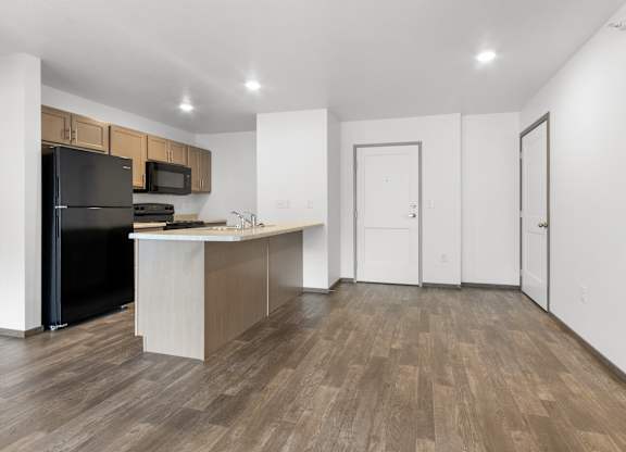 A kitchen with a black refrigerator and wooden floors.
