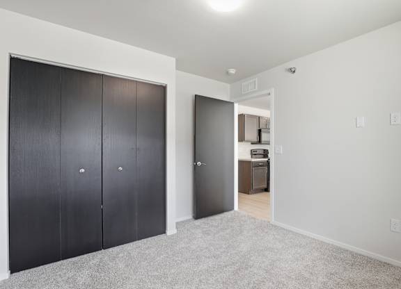 A room with a white wall and a carpeted floor with a black door on the left and a white door on the right.