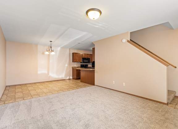 A spacious living room with a carpeted floor and a staircase on the right side.