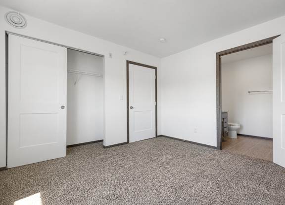 A room with white walls and a carpeted floor with four doors.