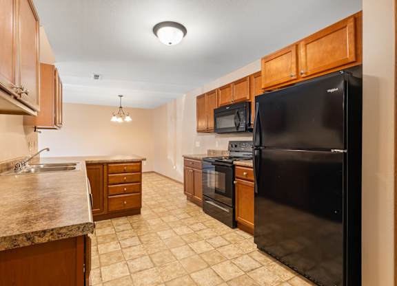A kitchen with a black refrigerator, brown cabinets, and a granite countertop.