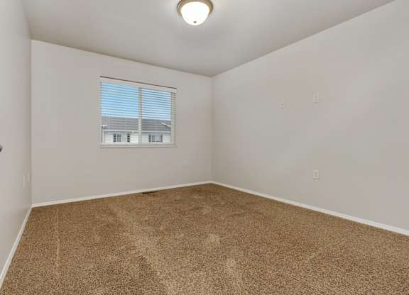 A room with a carpeted floor and a window with blinds.