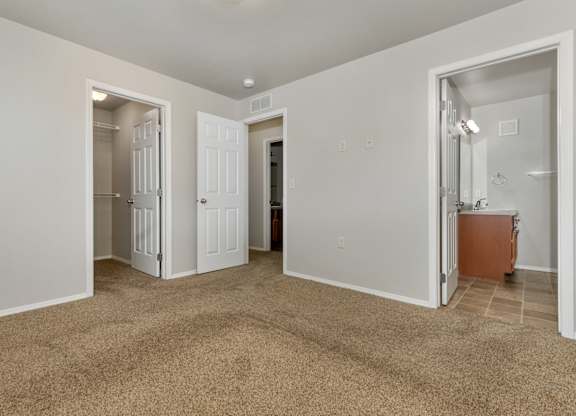 A room with carpeted floor and white walls with a doorway leading to another room.