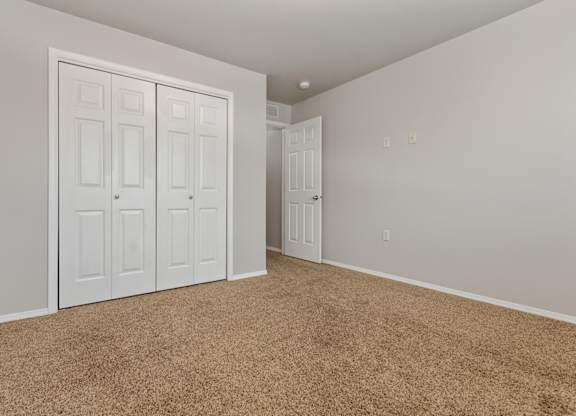 A room with carpeted floor and white walls with a white door and a white wardrobe with four doors.