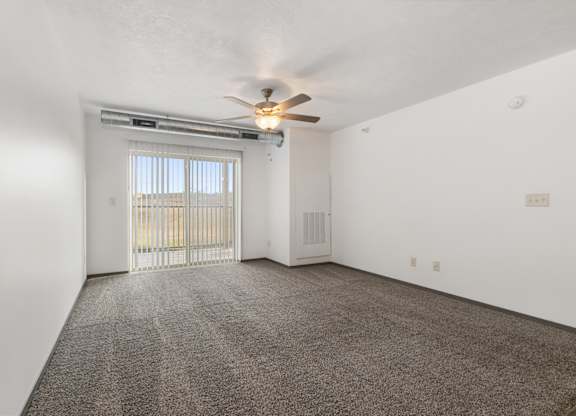 A room with a ceiling fan and a sliding glass door leading to a balcony.