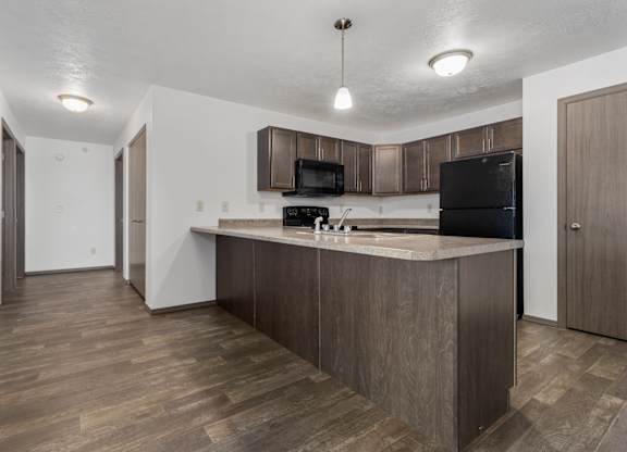 A kitchen with a wooden floor and a black fridge.