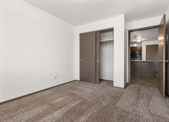 A room with a carpeted floor and a doorway leading to a kitchen.