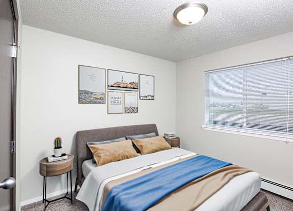 A bedroom with a bed, pillows, a small table, and pictures on the wall.
