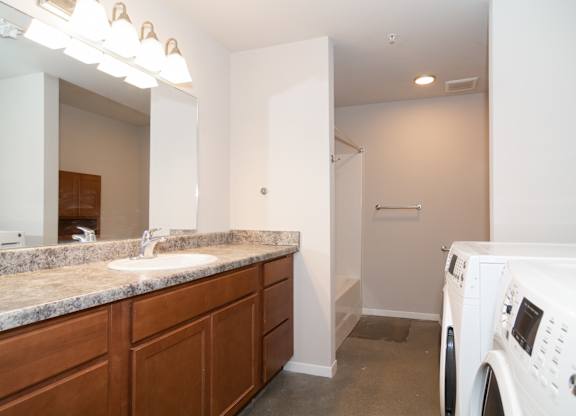 A white washing machine sits in a laundry room with a sink and mirror.