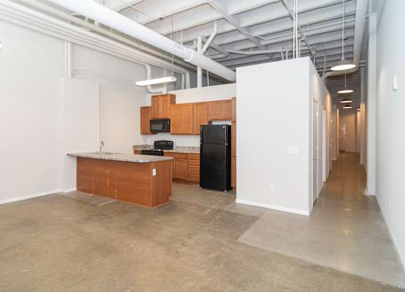 A kitchen area with a black fridge and microwave, a wooden counter, and a white wall.