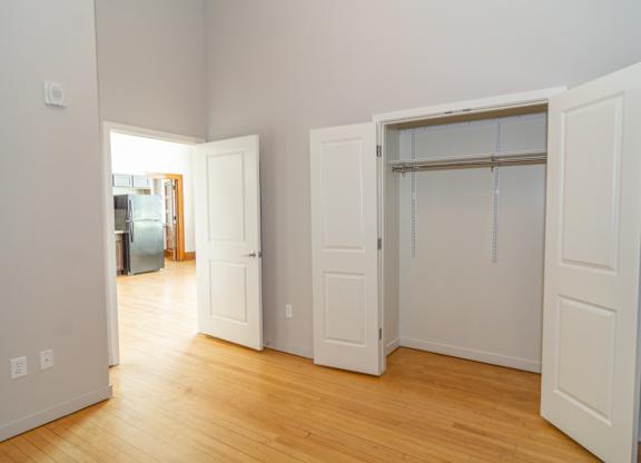 A room with white walls and wooden floors, with a doorway leading to another room.