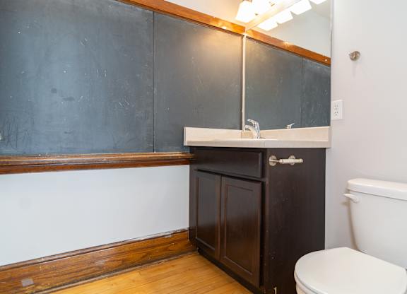 A bathroom with a toilet, sink, and wooden cabinet.