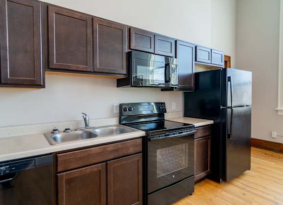 A black refrigerator is in a kitchen with wooden cabinets.