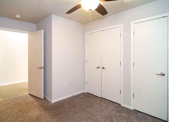 A room with a ceiling fan and three white doors.