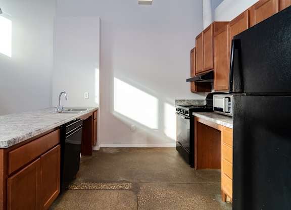 A kitchen with a black refrigerator and wooden cabinets.