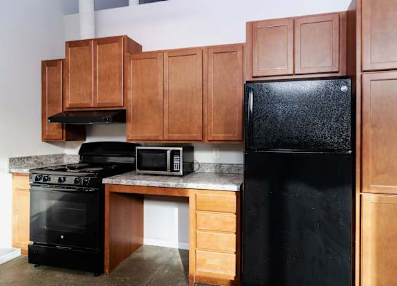 A black refrigerator sits in a kitchen with wooden cabinets.