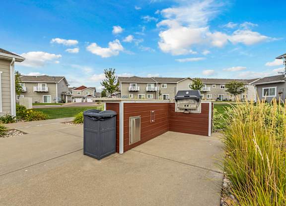 A residential area with a brown house and a grey trash bin.