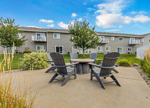 A concrete patio with a table and chairs in front of a grey apartment building.
