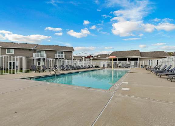A large swimming pool surrounded by lounge chairs and apartment buildings.