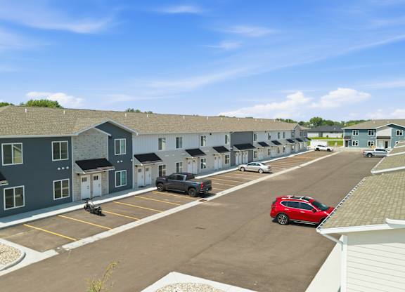 A red car is parked in a parking lot in front of a building.