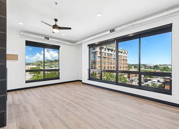 A room with a ceiling fan and a view of a building outside the window.