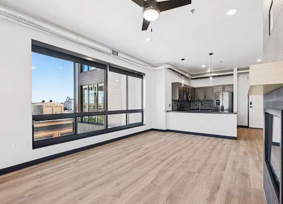 A spacious room with a ceiling fan and a view of the city through the windows.