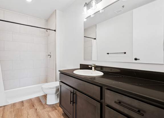 A bathroom with a white shower curtain, a white toilet, a sink with a mirror above it, and a black counter.