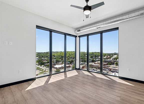 A room with a ceiling fan and large windows overlooking a cityscape.