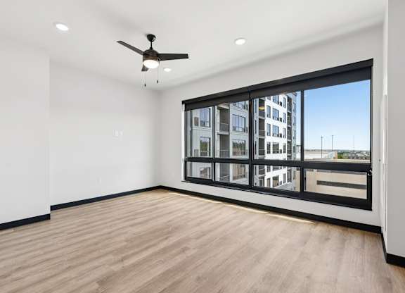 A room with a ceiling fan and a large window overlooking a cityscape.