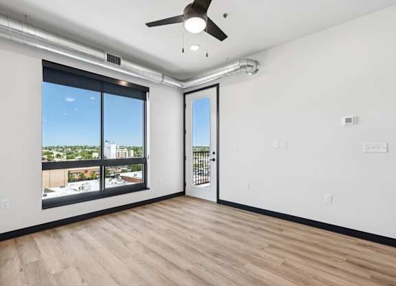 A room with a ceiling fan and a view of the city through the window.