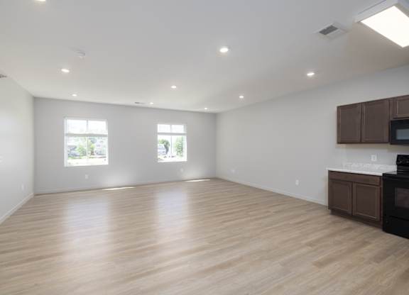 A spacious room with wooden flooring and two windows.