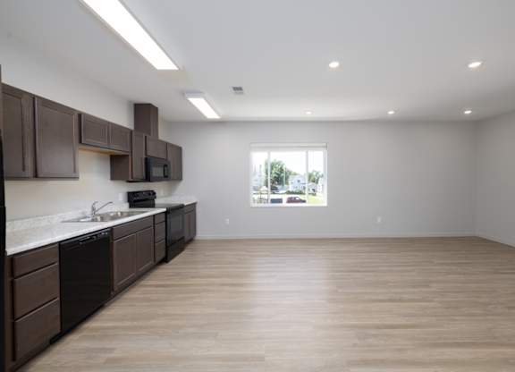 A kitchen with brown cabinets and a window overlooking a green landscape.