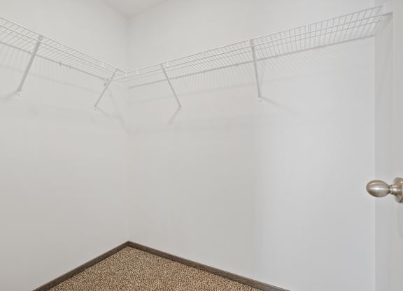 A white wall with a brown carpet and a silver door handle.