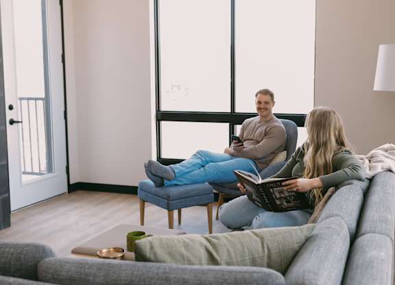 A man and a woman are sitting on a couch and a chair respectively, reading a book together.