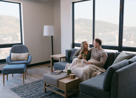 A couple is sitting on a couch in a living room with a view of the city.