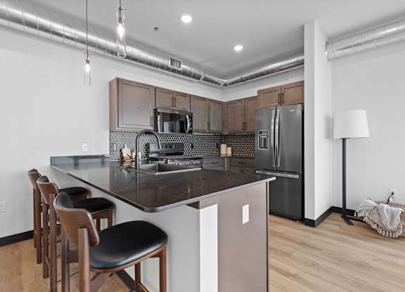A kitchen with a refrigerator, stove, and bar stools.