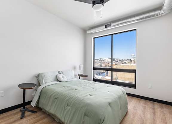 A bedroom with a bed, a small table, and a window overlooking a cityscape.
