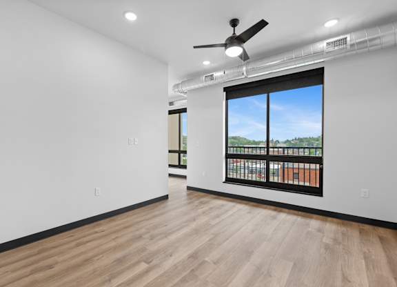 A room with a ceiling fan and a window overlooking a balcony.