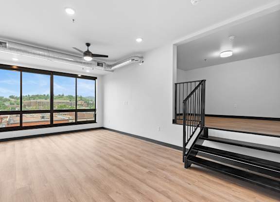 A room with a wooden floor, a staircase, and a ceiling fan.