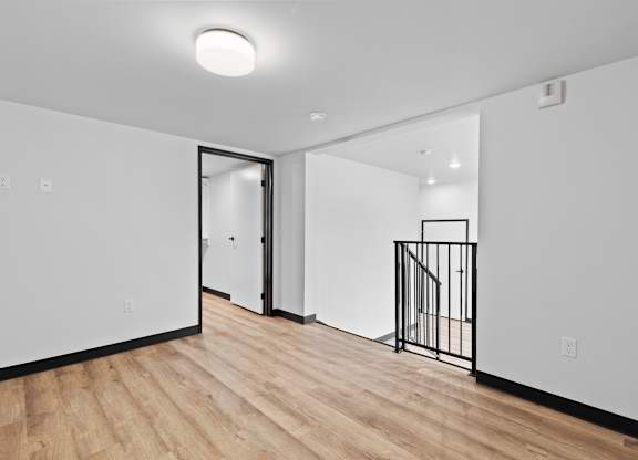 A room with a wooden floor and a white wall with a doorway leading to another room.