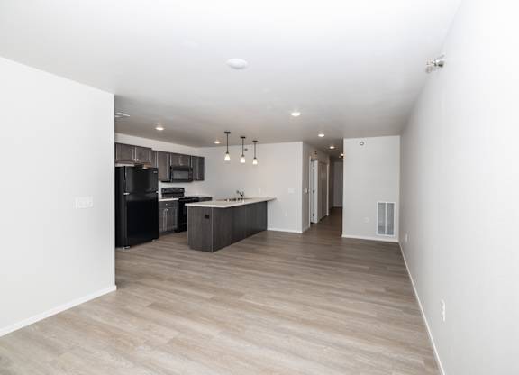 an empty living room and kitchen with white walls and wood flooring