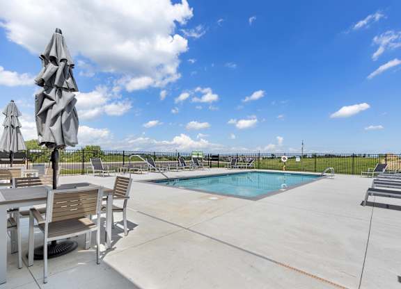 A pool area with a table and chairs and a blue pool.