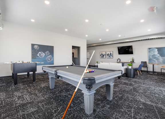 A pool table in a room with a chair and a plant.