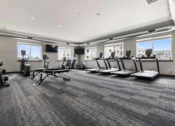 A gym with treadmills, elliptical machines, and a bench.