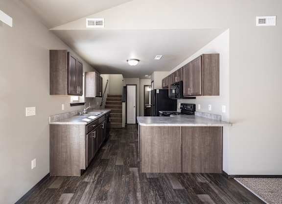 A kitchen with wooden floors and a black refrigerator.