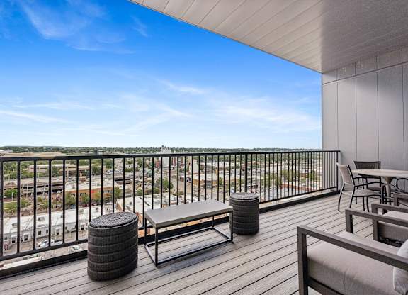 A balcony with a bench, table, and chairs overlooking a cityscape.